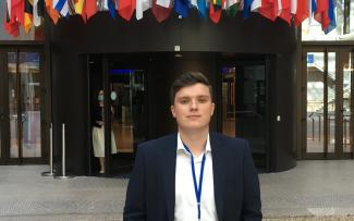 En bild på John Johansson. En man i kavaj som står utanför ingången till EU-parlamentet.